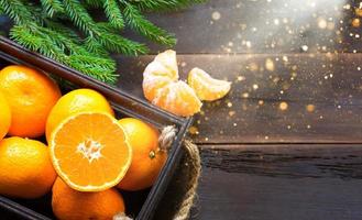 tangerinas frescas em caixa marrom sobre fundo de madeira com ramos de abeto verde. moldura, espaço de cópia, fragrância de férias e inverno, ano novo, natal. comida saudável, suco de laranja, vitrine. fatiar e cortar foto