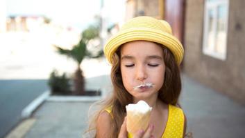 a criança come delicioso sorvete ao ar livre com prazer no verão, sujou a boca. uma garota com um chapéu amarelo e um vestido de verão no calor de um retrato de close-up foto