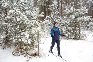 esquiador com uma mochila e chapéu com pompom com bastões de esqui nas mãos no fundo de uma floresta de neve. esqui cross-country na floresta de inverno, esportes ao ar livre, estilo de vida saudável, turismo de esportes de inverno. foto