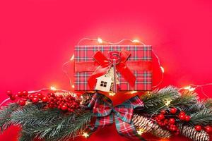 chave de casa com casa de chaveiro em um fundo festivo com árvore de natal, luzes de guirlandas. feliz ano novo fundo vermelho, presente, cartão de felicitações. compra, construção, realocação, hipoteca foto