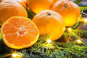 tangerinas frescas em luzes de guirlanda, em ramos de abeto e enfeites - fundo brilhante de ano novo. metade de uma laranja, aroma cítrico do feriado. natal, ano novo. espaço para texto. foto