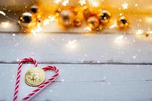 moeda bitcoin no coração de caramelo de cana doce com luzes de fadas e neve. natal, cartão de ano novo. criptomoeda, finanças, riqueza e investimento. espaço de cópia