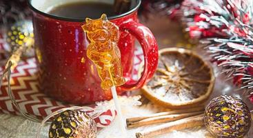 dois pirulitos na vara em forma de símbolo do ano novo 2021 - touro na decoração de natal de fundo com uma xícara vermelha de chá. guirlandas, canela e laranja seca - atmosfera de aconchego, conforto e magia. foto