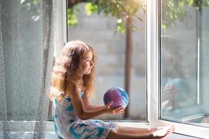 a garota na janela da casa está segurando uma lâmpada em forma de planeta, um globo. paz, ecologia, meio ambiente, pacífico
