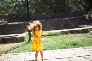 uma garota turista em um chapéu amarelo e vestido dançando ao longo da rua da cidade velha de pedra com uma fortaleza. passeio turístico. foto