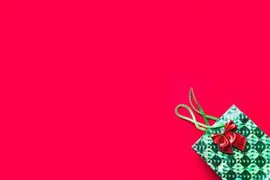 pacote verde com um presente e um laço em um fundo vermelho com copyspace. um presente para o ano novo, natal, aniversário, aniversário, festa. Shopping foto