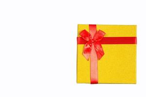 a caixa de presente dourada é amarrada com uma fita vermelha com um laço em um fundo branco e isolada. copie o espaço. presente para natal, ano novo, aniversário, feriado. foto