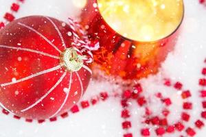 bola vermelha de natal na neve branca natural com miçangas quadradas e vela acesa em um castiçal de vidro. natal, ano novo ao ar livre. queda de neve, clima festivo de contos de fadas e magia, decoração de rua. foto