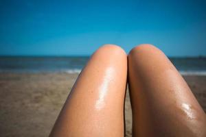 uma mulher na praia esfrega os pés com protetor solar de um tubo laranja. cuidados com a pele, proteção uv, protetor solar. férias na praia foto