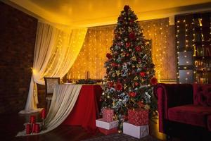 interior de natal da sala escura da casa. árvore de natal, luzes de guirlandas nas paredes, armário da biblioteca, livros nas prateleiras. interior de luxo. ano novo, bolas vermelhas e douradas. foto