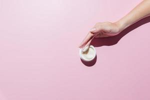 mão de mulher com um creme em um fundo rosa. mãos preparadas, unhas curtas naturais, cosméticos m.ockup foto