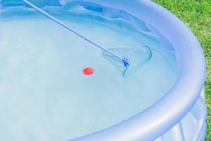 limpeza da piscina do jardim. menino tenta pegar bola vermelha com rede skimmer foto