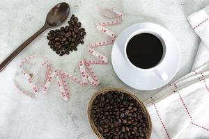 xícara de café e fundo de grãos de café com torneira de medida na mesa branca.