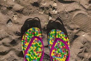 chinelos multicoloridos na areia com forma de coração desenhada. conceito de férias foto