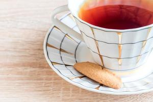 xícara de chá preto com saboroso biscoito crocante na mesa de madeira foto