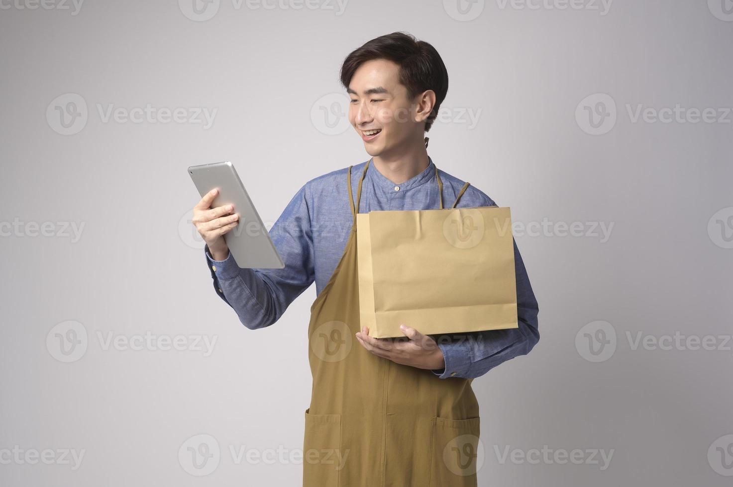 Porträt eines jungen asiatischen Mannes mit Schürze, der eine Tablette über weißem Hintergrund hält Studio, Unternehmerkonzept foto