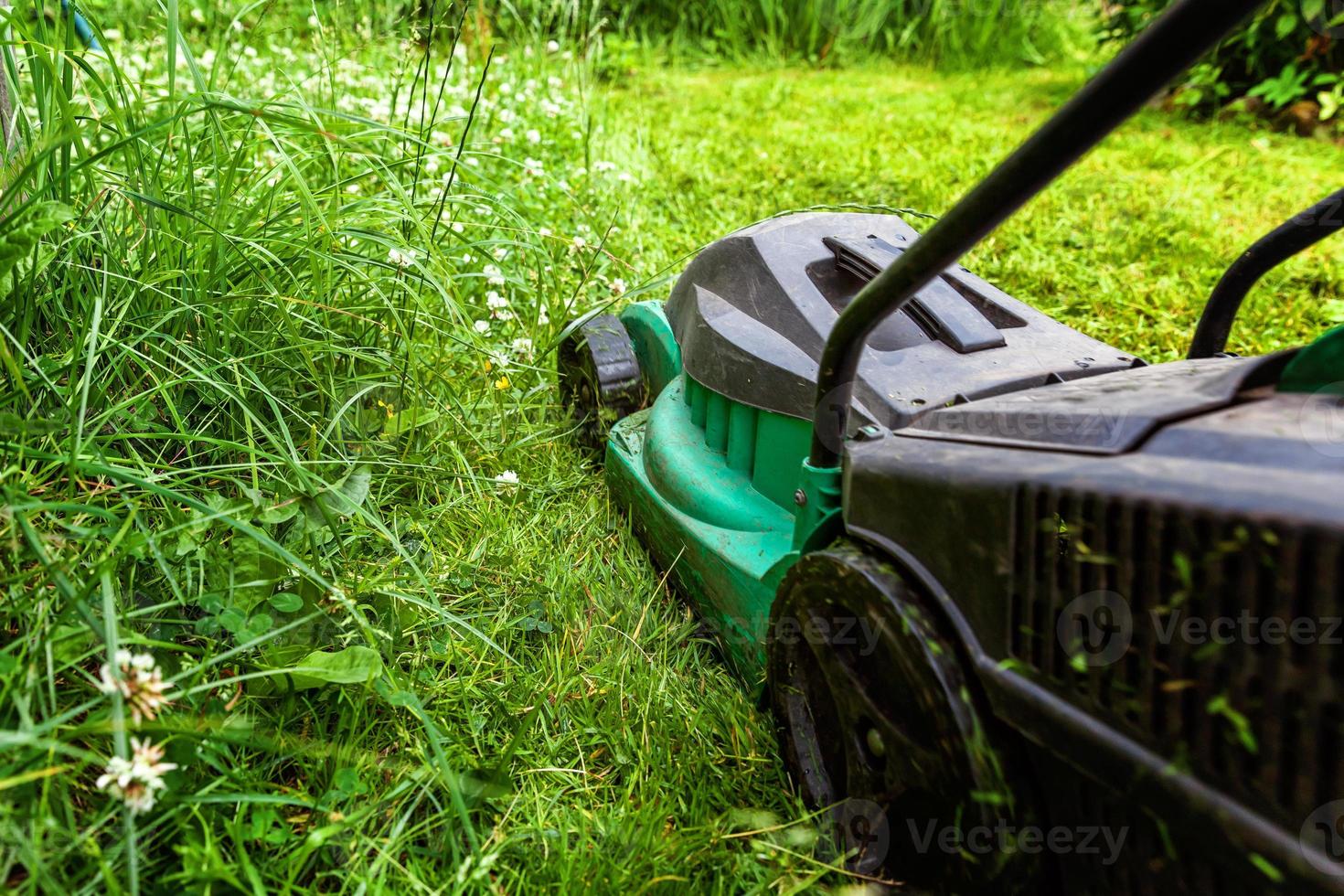 Mann schneidet grünes Gras mit Rasenmäher im Hinterhof. Gartenland-Lifestyle-Hintergrund. schöne aussicht auf frischen grünen rasen im sonnenlicht, gartenlandschaft im frühling oder in der sommersaison. foto