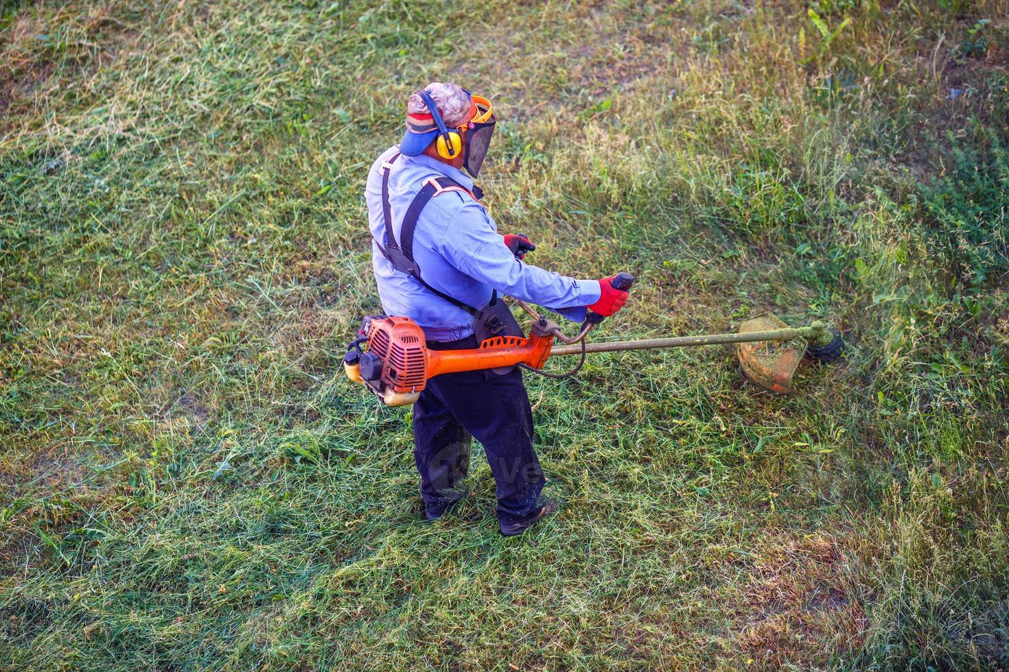 draufsicht rasenmäher mann arbeiter schneiden trockenes gras mit rasenmäher. foto