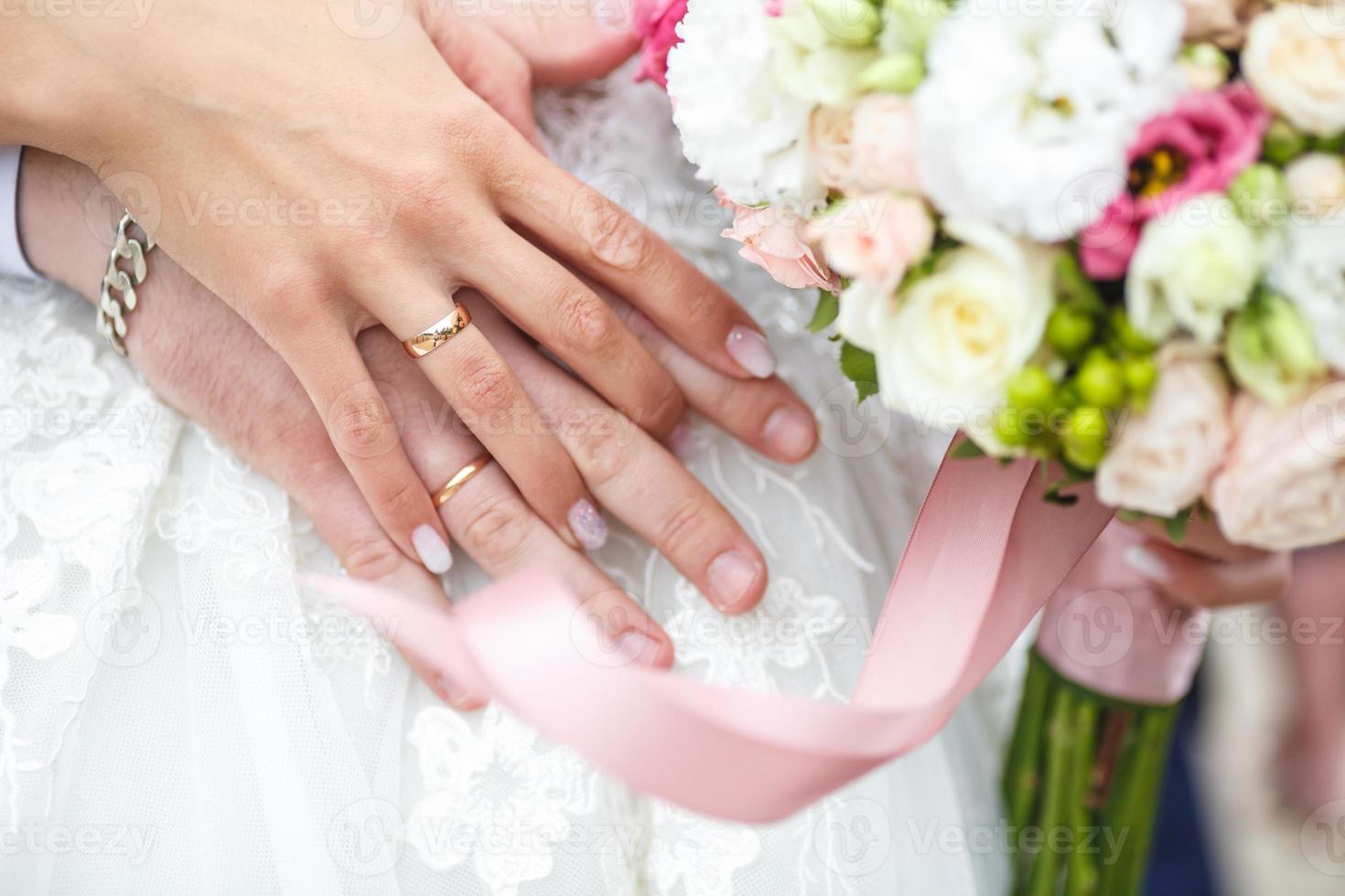 bräutigam umarmt die braut mit hochzeitsstrauß aus roten weißen rosen. Ringe an den Händen des frisch verheirateten Paares foto