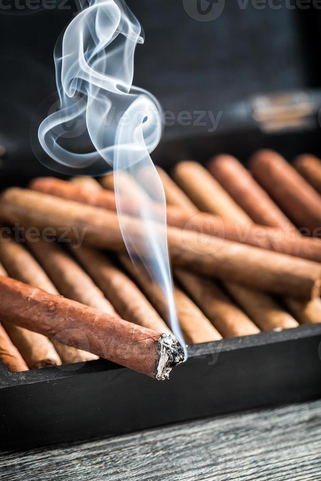 brennende Zigarre auf hölzernem Humidor voll mit Zigarren foto