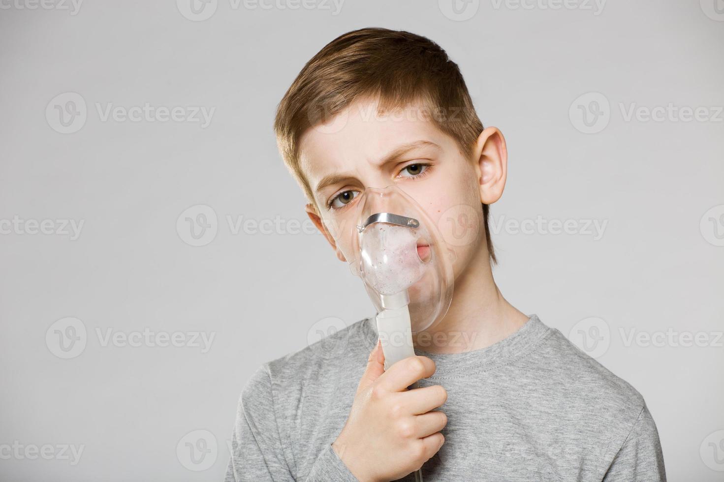 Junge über grauem Hintergrund, der Inhalatormaske hält foto