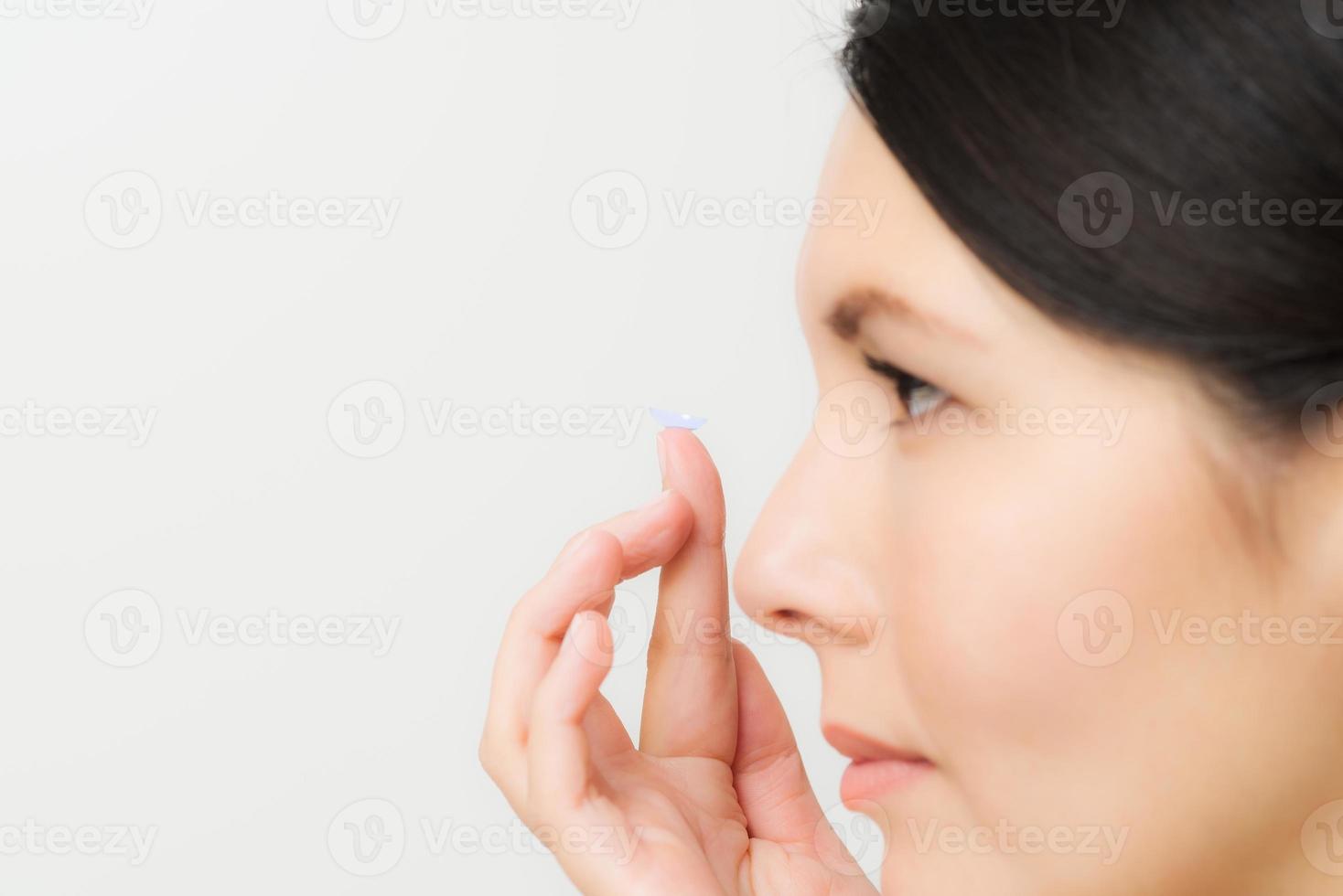 Frau im Begriff, eine Kontaktlinse in ihr Auge zu setzen foto