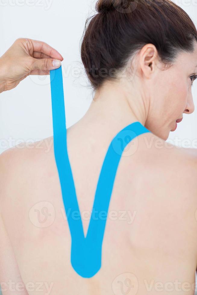 Physiotherapeut bringt blaues Kinesio-Klebeband auf den Rücken des Patienten an foto