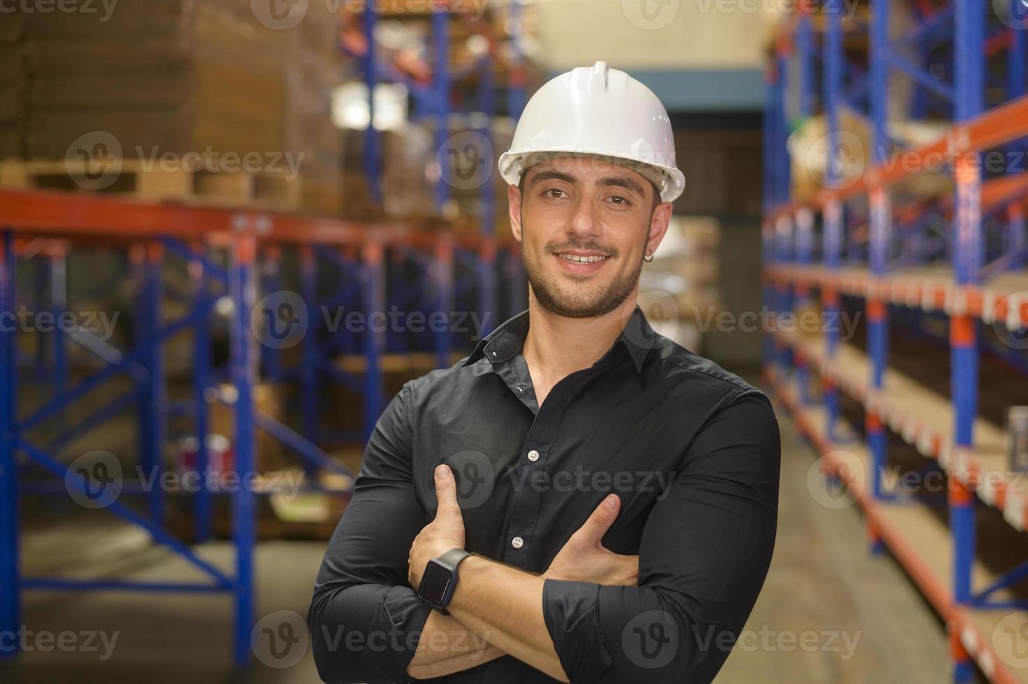 porträt eines jungen kaukasischen männlichen arbeiters mit helm in der modernen lagerlagerung des einzelhandelsgeschäfts foto