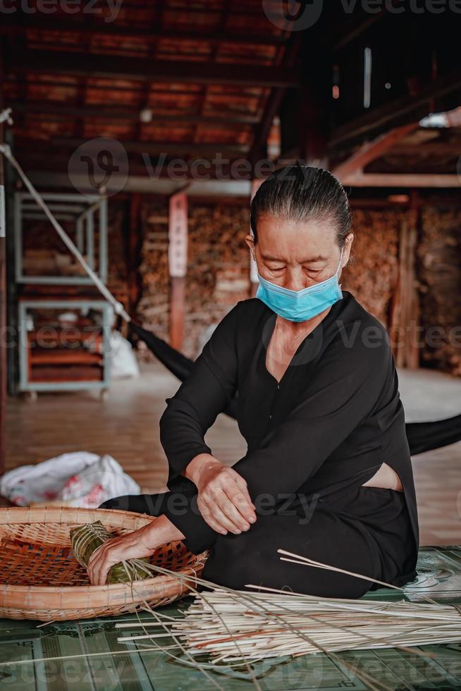 fokus alte frau mit traditionellem vietnamesischem kleid ao ba ba machen, verpacken tet kuchen, das vietnamesische mondneujahr tet essen im freien von händen. foto