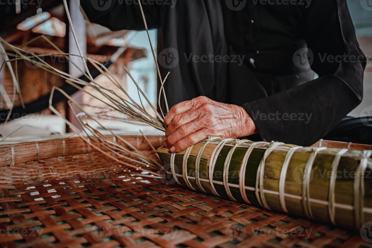 fokus alte frau mit traditionellem vietnamesischem kleid ao ba ba machen, verpacken tet kuchen, das vietnamesische mondneujahr tet essen im freien von händen. foto