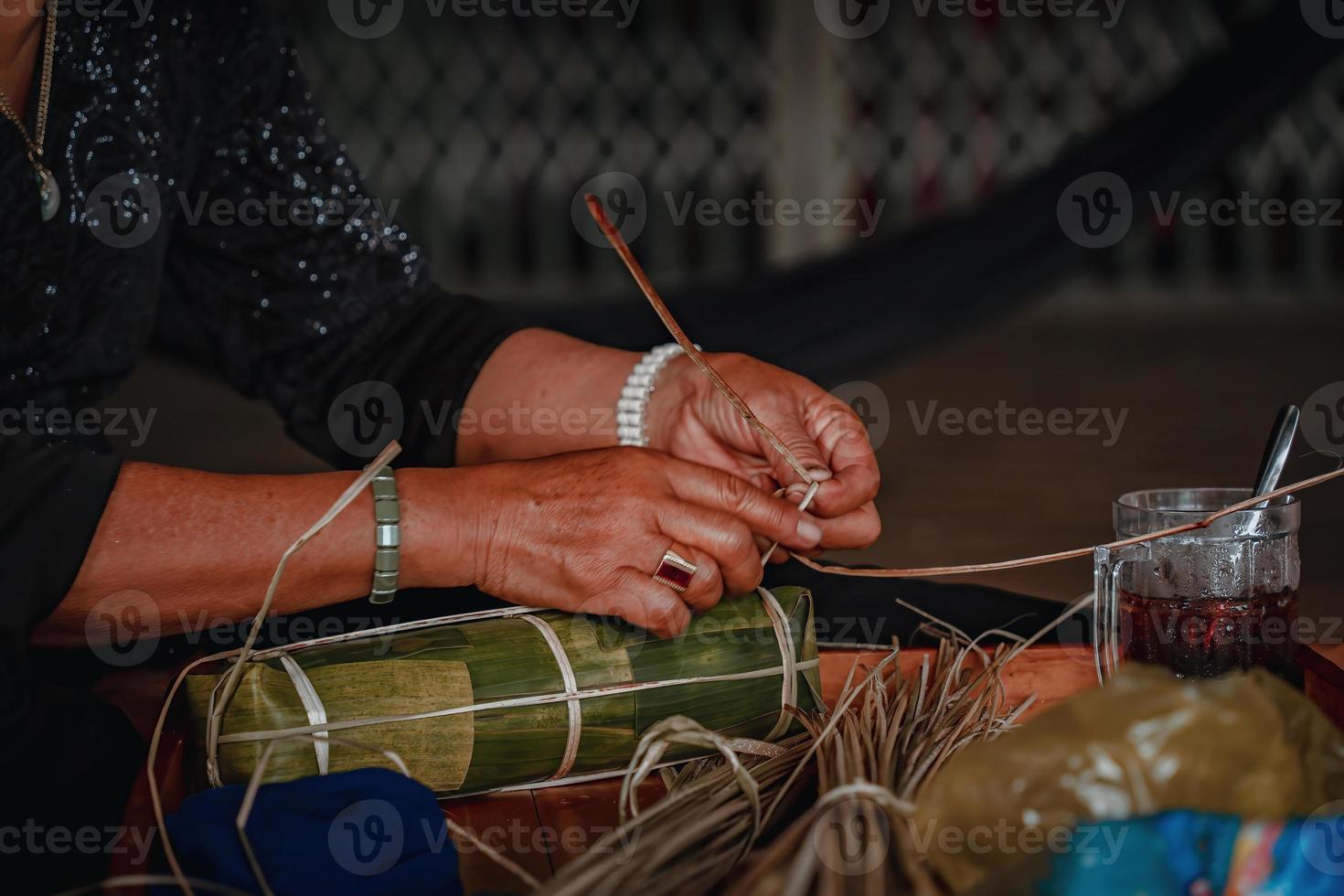 fokus alte frau mit traditionellem vietnamesischem kleid ao ba ba machen, verpacken tet kuchen, das vietnamesische mondneujahr tet essen im freien von händen. foto