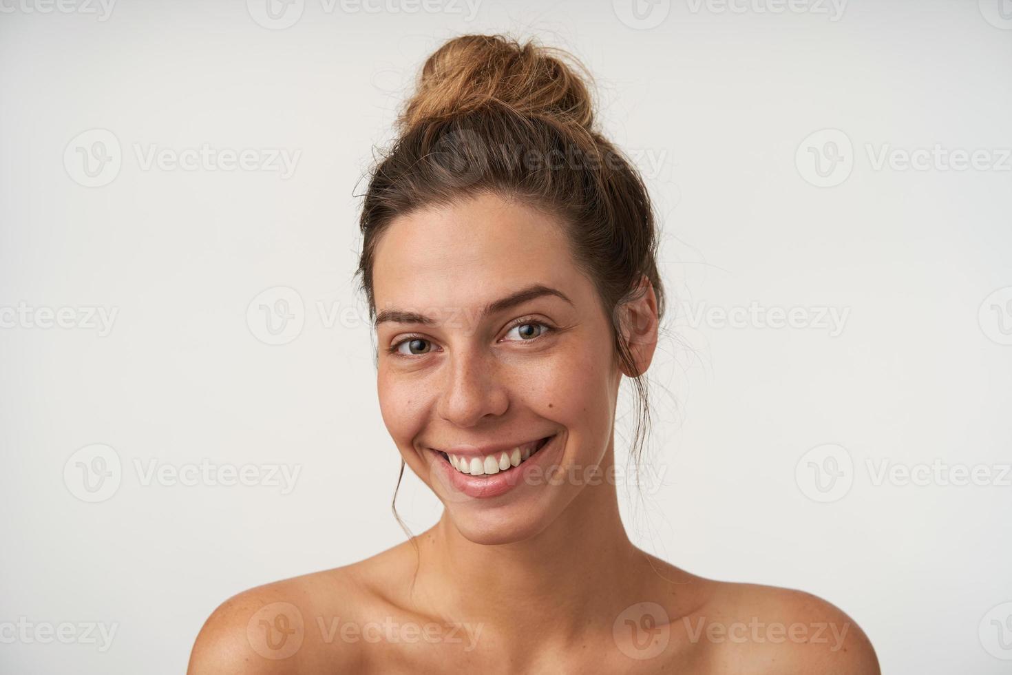 Innenporträt einer fröhlichen jungen Frau, die aufrichtig in die Kamera lächelt, ohne Make-up schön aussieht und auf weißem Hintergrund steht foto