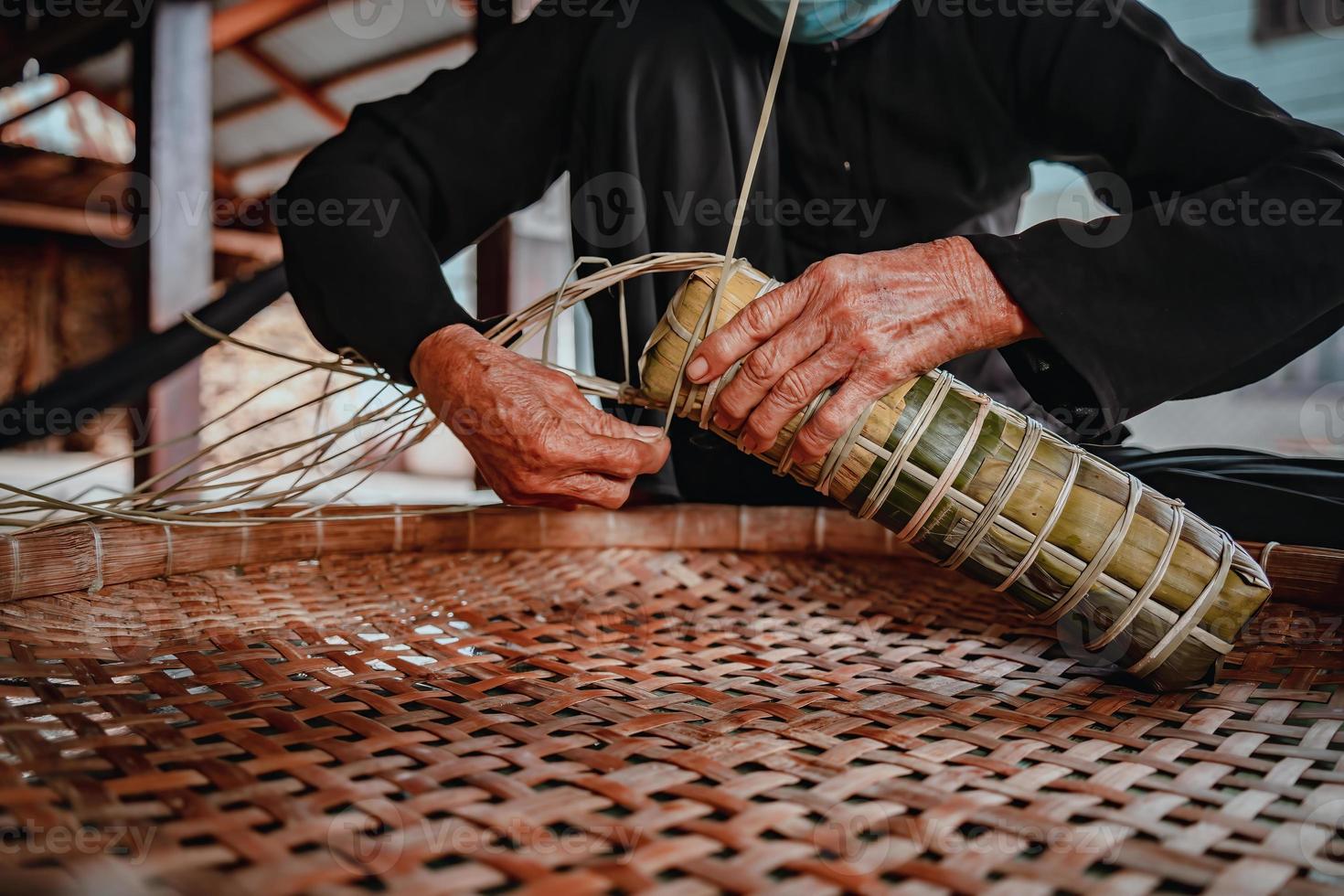 fokus alte frau mit traditionellem vietnamesischem kleid ao ba ba machen, verpacken tet kuchen, das vietnamesische mondneujahr tet essen im freien von händen. foto