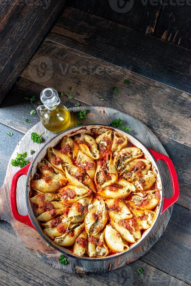 Manicotti-Nudelschalen mit Spinat, Ricotta, Mozzarella-Käse in Tomatensauce in roter Pfanne in rustikaler Umgebung flach gelegt foto