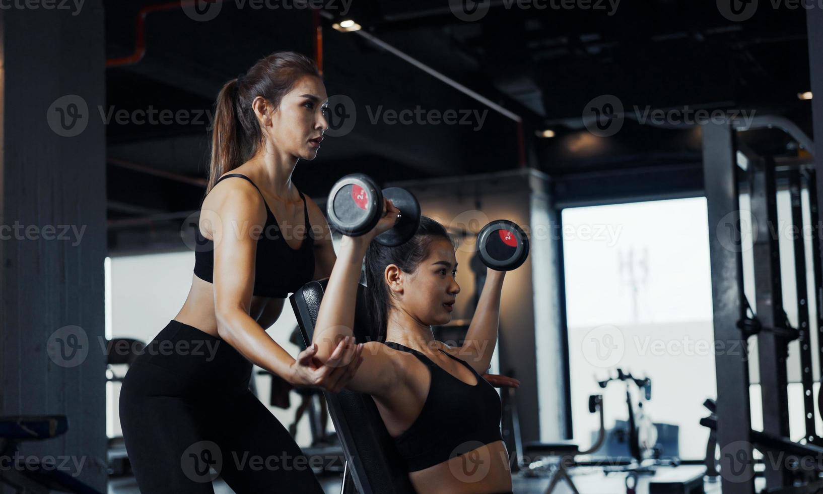 sportliches mädchen, das mit hilfe ihres persönlichen trainers im fitnessstudio gewichtsübungen macht. foto