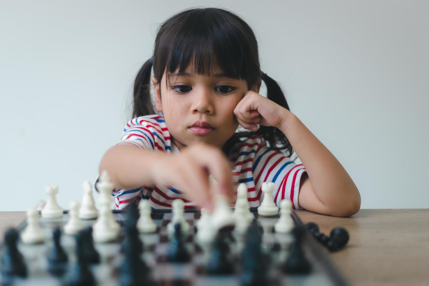 asiatisches kleines mädchen, das zu hause schach spielt. ein schachspiel foto