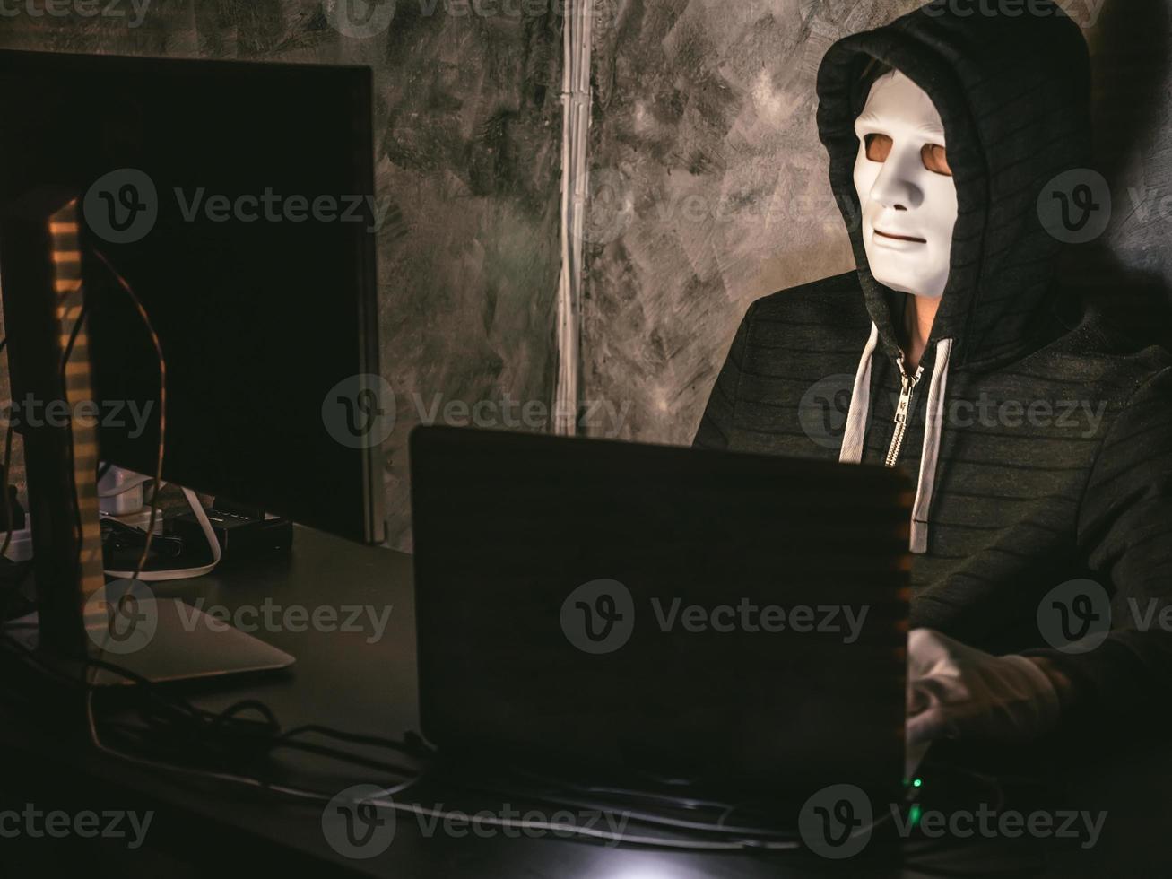 Computerhacker - Mann im Kapuzenshirt mit Maske, der Daten vom Laptop stiehlt foto