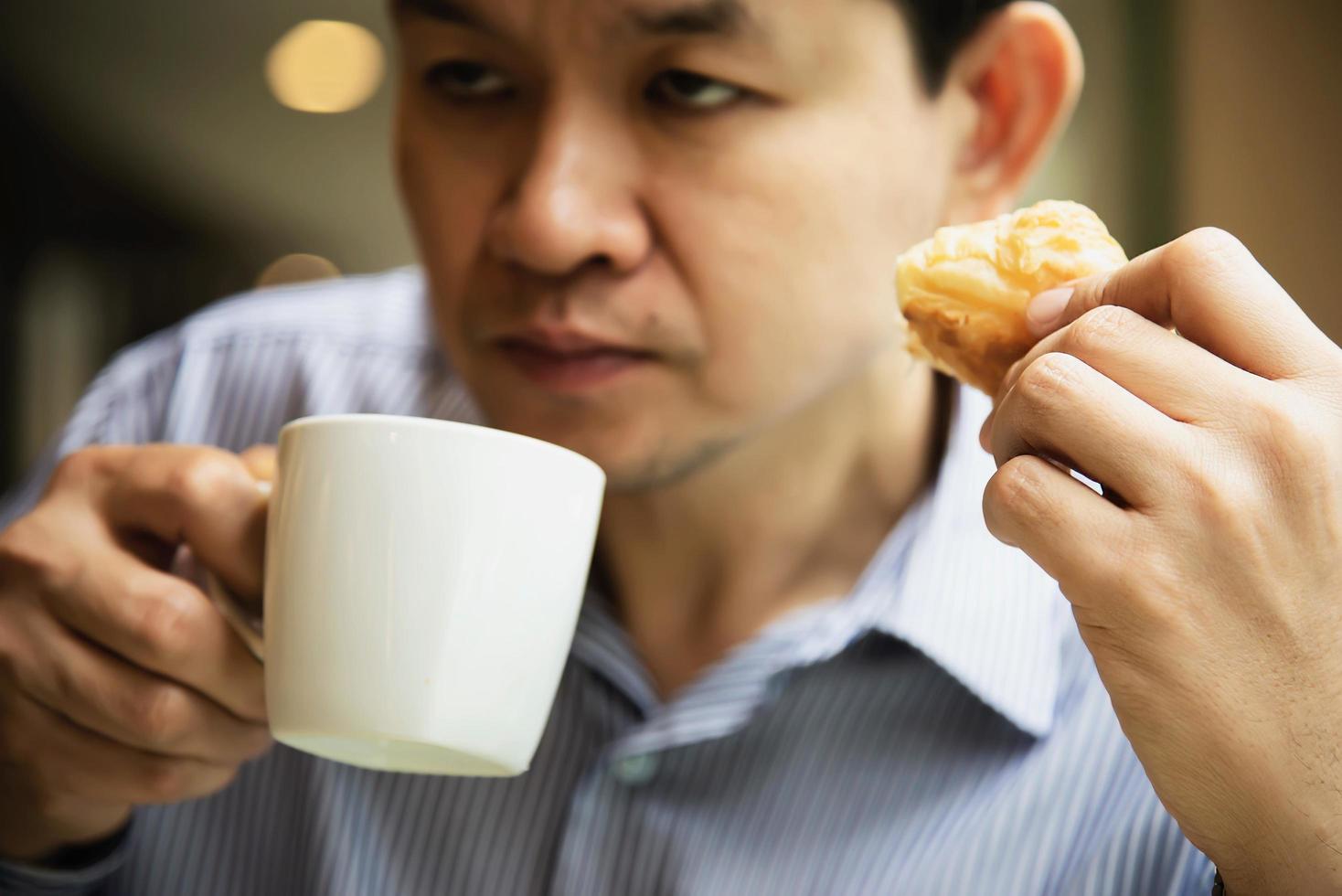 schläfriger mann, der kaffee mit brot trinkt - menschen mit koffeinkaffeegetränkkonzept foto