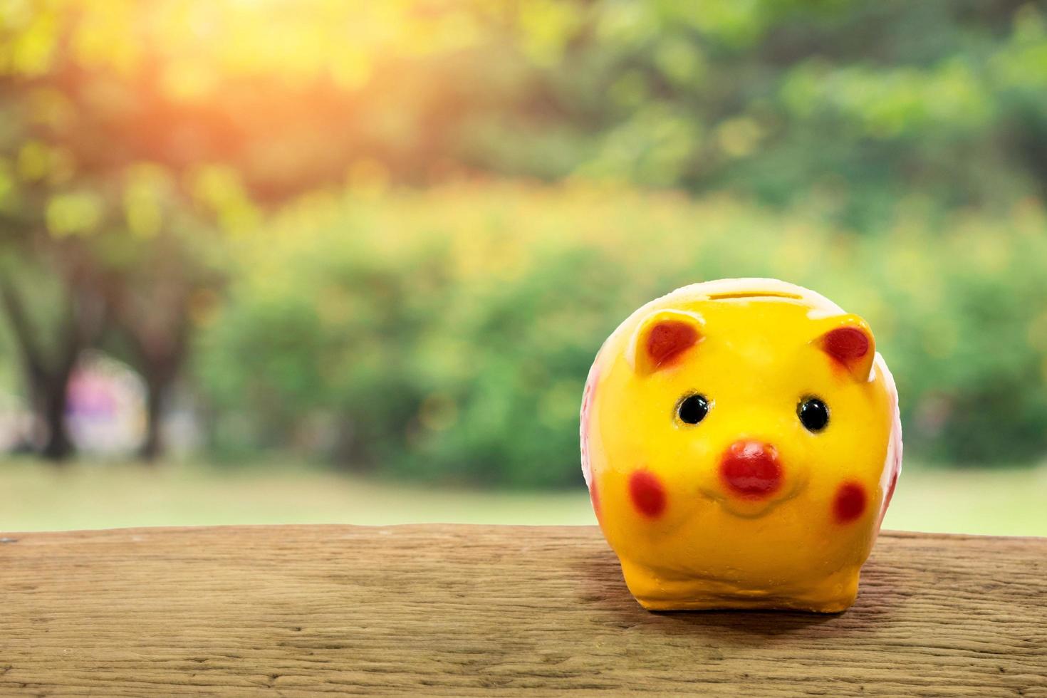 Gelbes Sparschwein auf Holztisch über verschwommenem natürlichem Bokeh-Hintergrund. Sparen, Geldkonzept foto