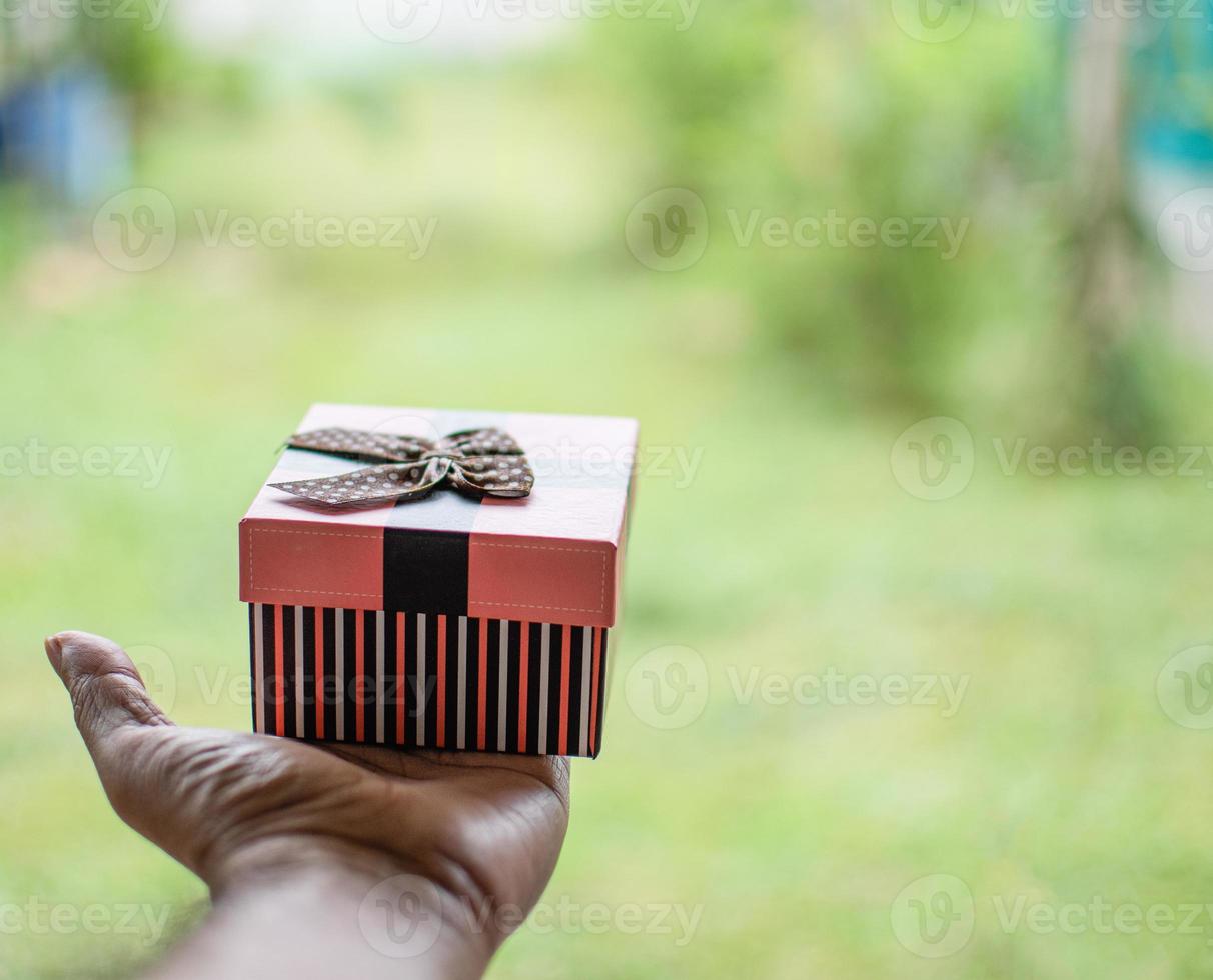 Die eine linke Hand hält eine Geschenkbox mit verschwommenem Hintergrund und Copyspace oben und rechts. Dieses Bild ist eine Nahaufnahme und ist Landschaft. foto