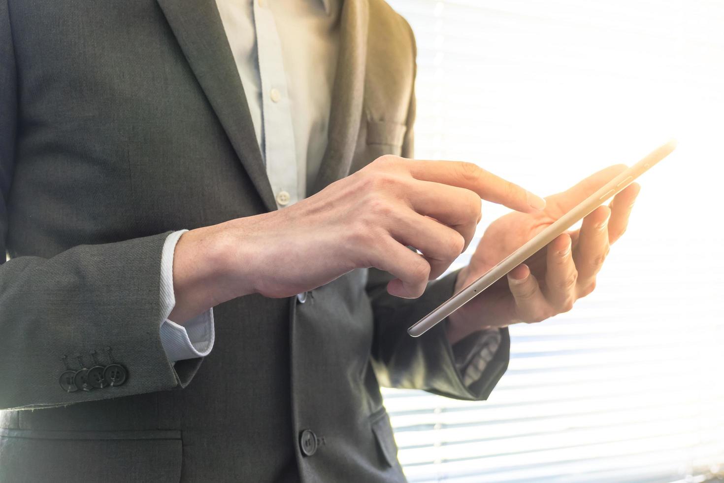 Nahaufnahme eines Geschäftsmannes, der ein Tablet-Gerät verwendet, während er an einem Fenster in einem Büro steht foto