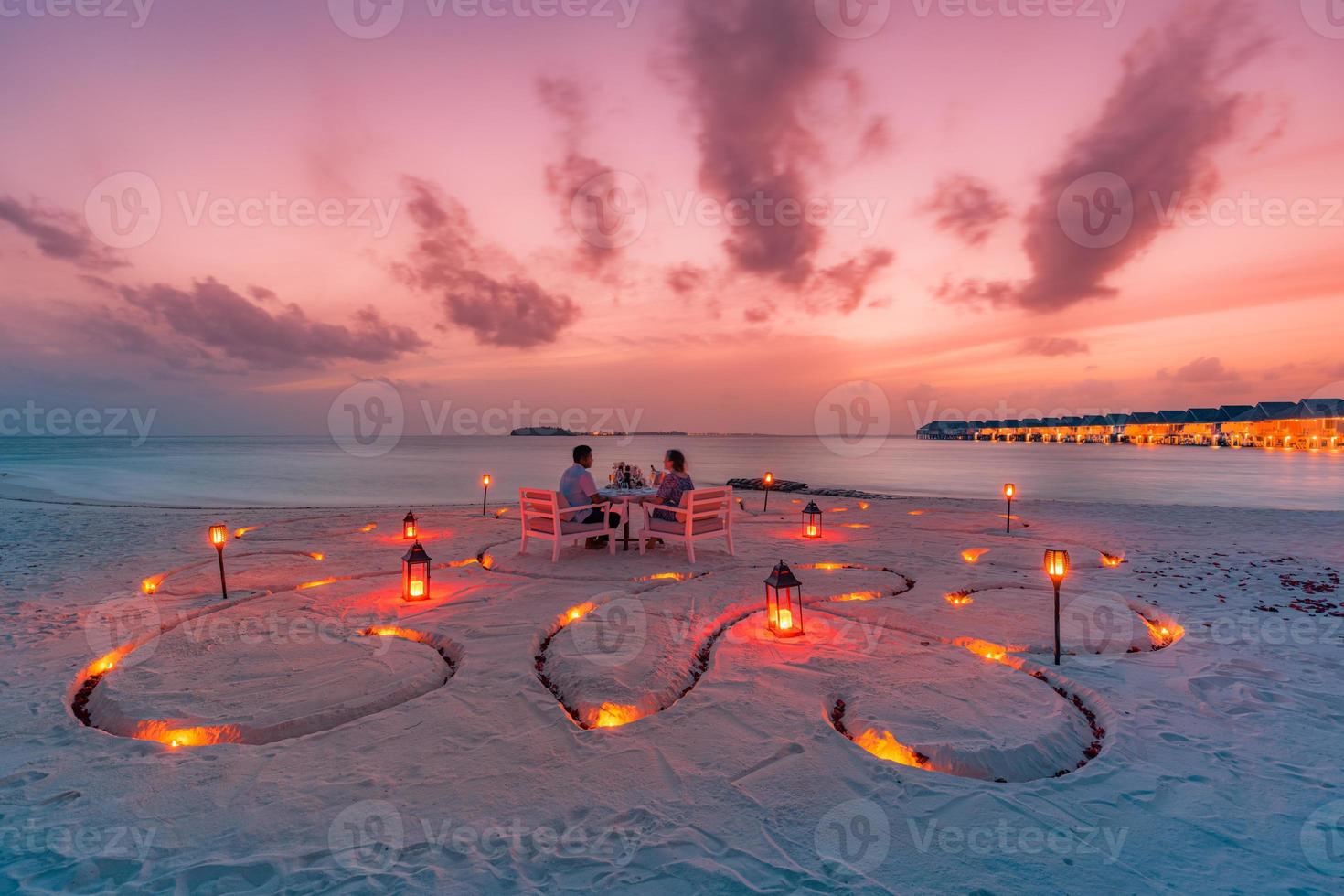 Destination Dining, Flitterwochen, Jubiläum. erstaunlicher romantischer Dinner-Strand auf Holzterrasse mit Kerzen unter Sonnenuntergang. Romantik und Liebe, Luxus-Dinner, exotische Tischdekoration mit Meerblick foto