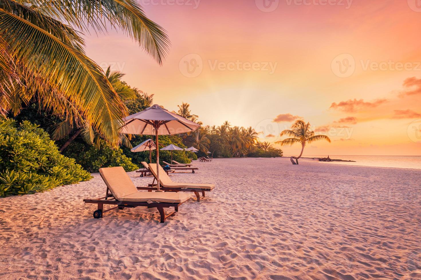 wunderschöne tropische Sonnenuntergangslandschaft, zwei Sonnenliegen, Liegestühle, Sonnenschirm unter Palmen. weißer Sand, Meerblick mit Horizont, bunter Dämmerungshimmel, Ruhe und Entspannung. inspirierendes Strandresorthotel foto