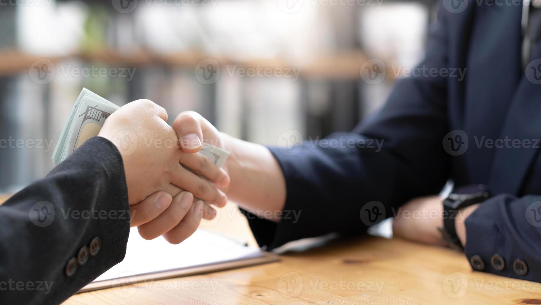 eine asiatische rechtsanwältin oder geschäftsrechtsberaterin am schreibtisch erhält geld und schüttelt ihrem männlichen klienten die hand. beschnittenes Bild foto