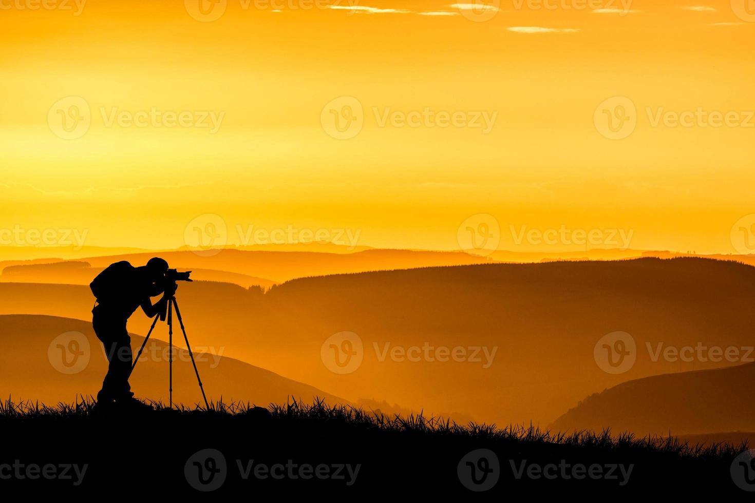 Die Silhouette eines professionellen Fotografen konzentriert sich auf das Fotografieren auf einer wunderschönen Wiese. foto