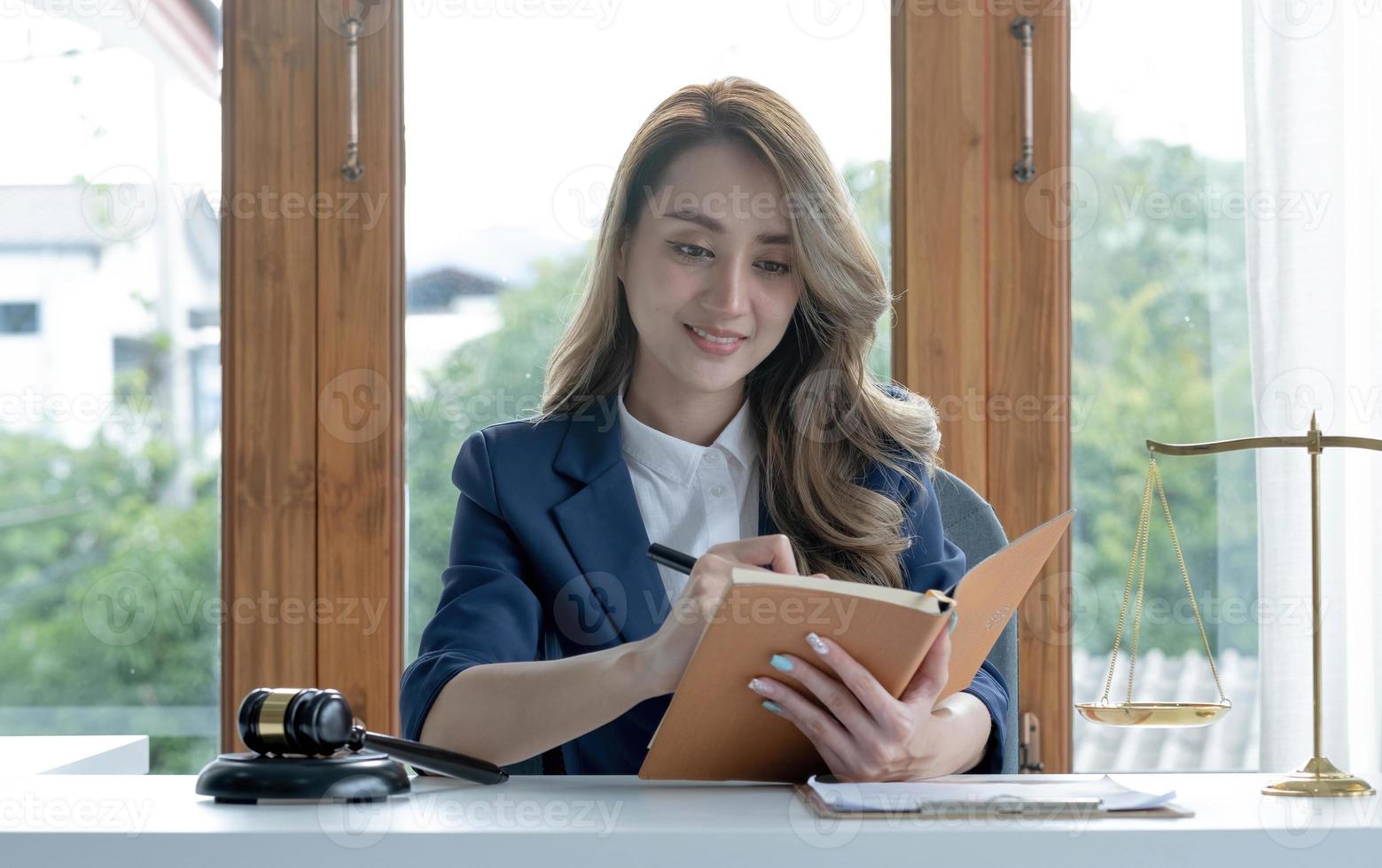 Selbstbewusste und erfolgreiche junge asiatische Rechtsanwältin oder Unternehmensrechtsberaterin, die ein Gesetzbuch liest oder etwas auf ihr Notizbuch an ihrem Schreibtisch schreibt. foto