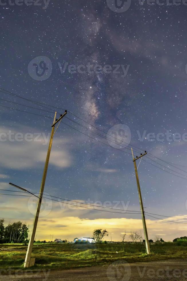 Strommasten in der nächtlichen Landschaft, der Himmel mit Sternen und wunderschönen Taro-Szenen, Wolken unter dem Horizont über dem Gras foto