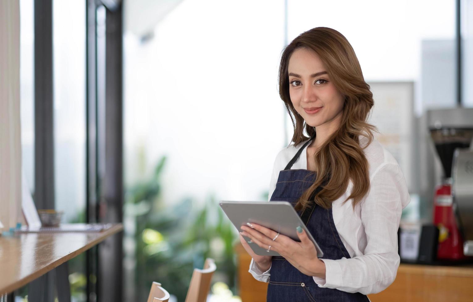 Startup erfolgreicher Kleinunternehmer SME Schönheitsmädchen steht mit Tablet-Smartphone im Café-Restaurant. Porträt der Barista-Café-Besitzerin mit asiatischer Bräune. KMU-Unternehmer-Verkäufer-Geschäftskonzept foto