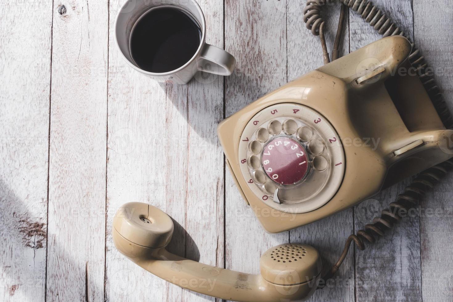 Draufsicht des alten Telefons mit Kaffeetasse auf weißem Holztischhintergrund. foto