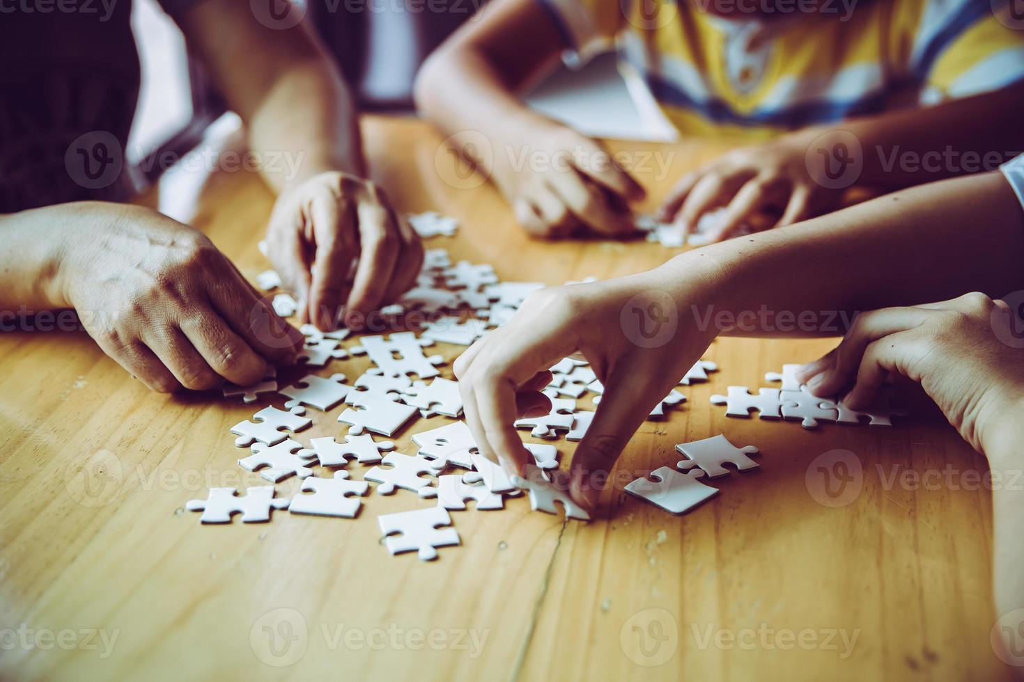 Hände einer Person, kleines Kind und Elternteil, die zu Hause zusammen auf einem Holztisch ein Puzzlespiel spielen, Konzept für die Freizeit mit der Familie, Spiel mit der Entwicklung, Bildung und Spaß der Kinder. foto